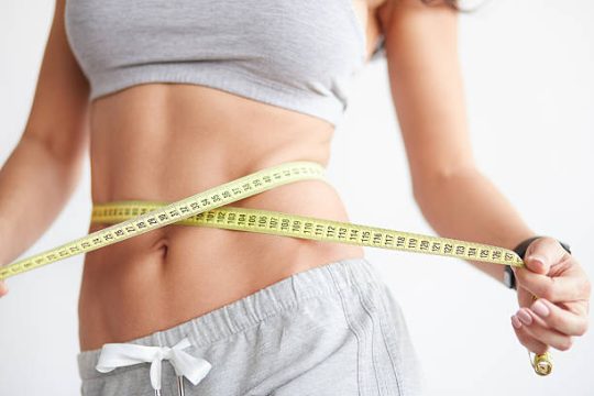 Slim girl with centimeter on white. Closeup woman measuring her waist with tape. Weight loss concept